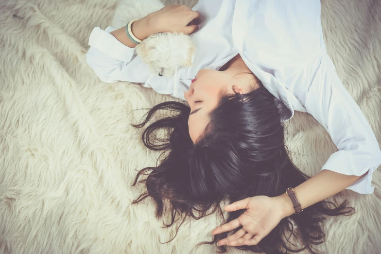 a woman laying on a fur rug with her eyes closed, pexels contest winner, young woman with long dark hair, wearing white pajamas, gif, hand