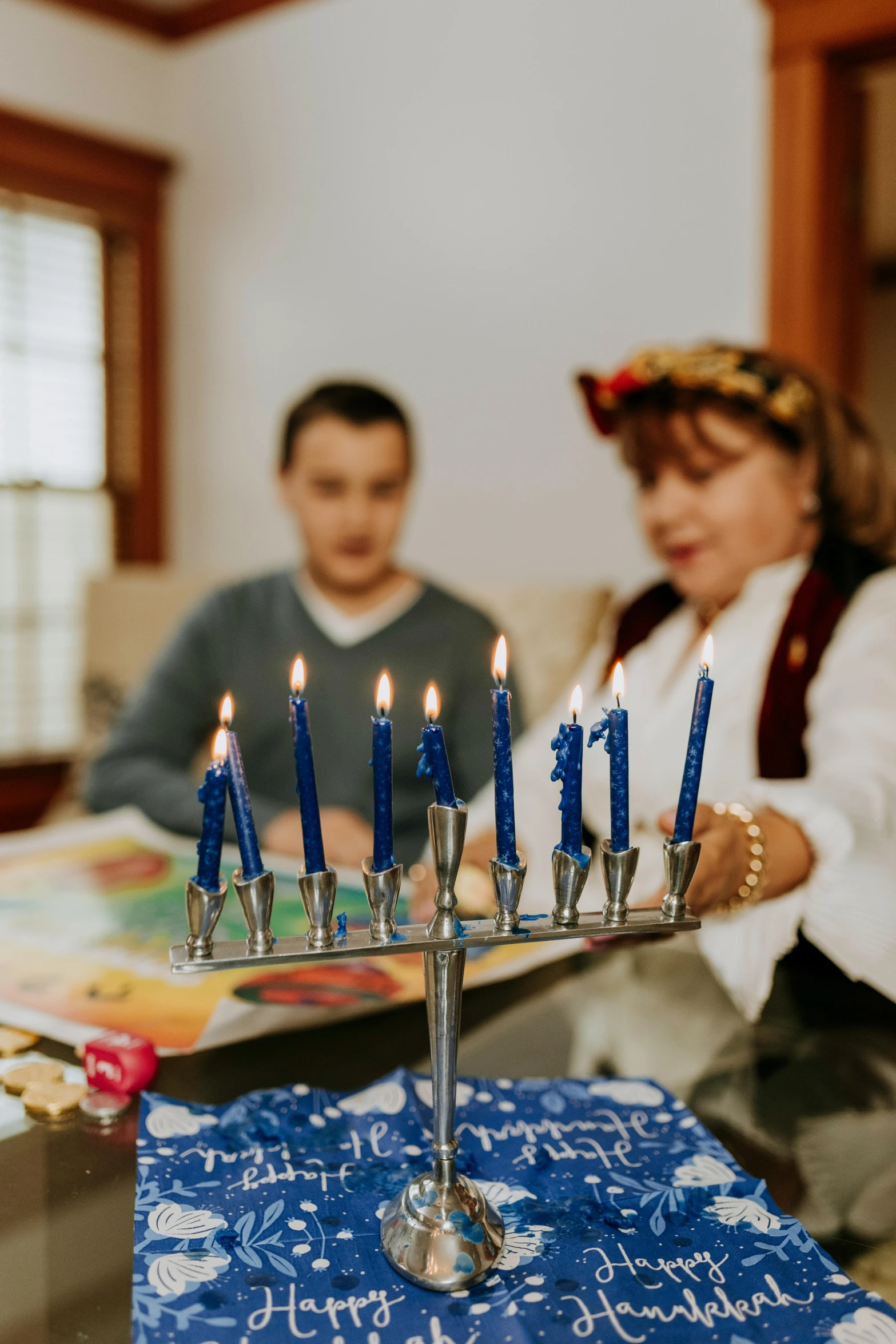 a group of people sitting around a table with a menorah, during the day, holiday season, blue and silver, kids