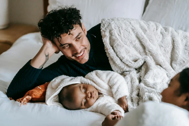 a man laying on top of a bed next to a baby, by Carey Morris, pexels contest winner, renaissance, mixed race, handsome male, happy cozy feelings, covered in robes