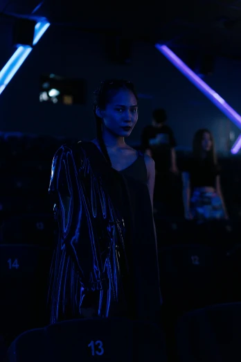 a man standing in front of a crowd of people, a hologram, by Robbie Trevino, photograph of a techwear woman, fashion studio lighting, [ theatrical ], black and blue and purple scheme
