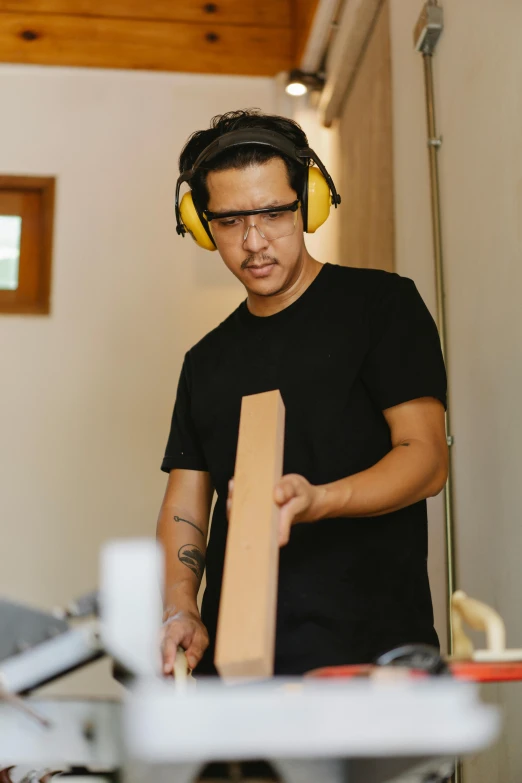 a man using a table saw to cut a piece of wood, an album cover, arbeitsrat für kunst, wearing black headphones, profile image, asian male, trending photo