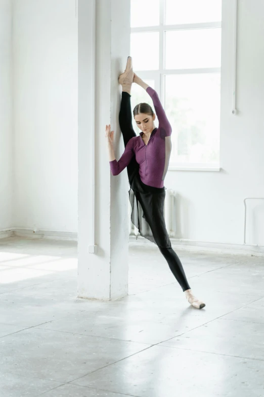 a woman in a purple shirt is leaning against a wall, a picture, by Elizabeth Polunin, shutterstock, arabesque, wearing black tight clothing, full - length photo, square, daniil kudriavtsev