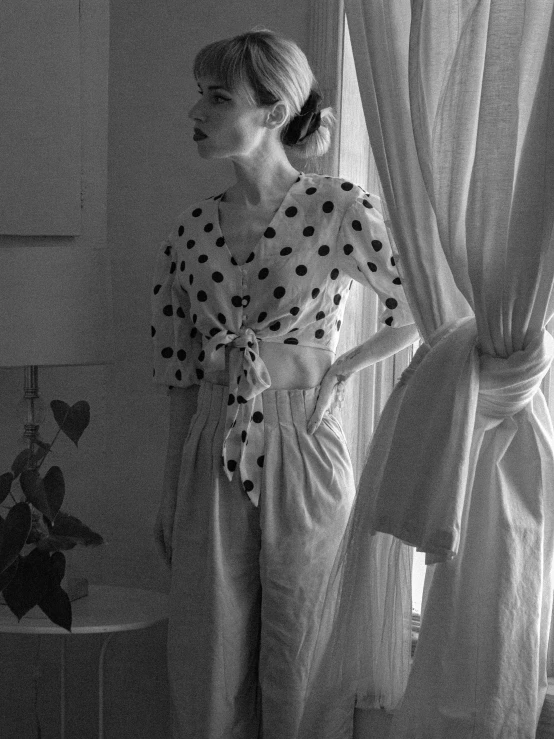 a black and white photo of a woman standing in front of a window, a black and white photo, by Pamela Ascherson, polkadots, vintage shirt, by greg rutkowski, anna nikonova aka newmilky