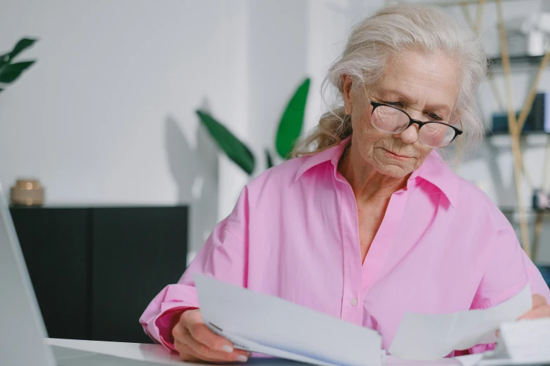 a woman sitting at a table reading a book, a photo, gray haired, profile image, pink glasses, document photo