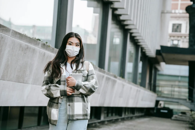 a woman wearing a face mask standing in front of a building, a picture, trending on pexels, asian girl with long hair, healthcare, wearing acne outfit, student
