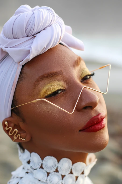 a woman wearing glasses and a turban on the beach, an album cover, inspired by Thomas Blackshear, trending on pexels, triangle makeup, gold wires, closeup - view, geometrically perfect