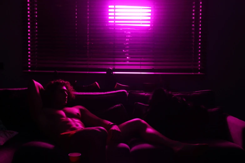 two people sitting on a couch in a dark room, inspired by Nan Goldin, bright pink purple lights, synthwave image, 33mm photo, pink sunlight