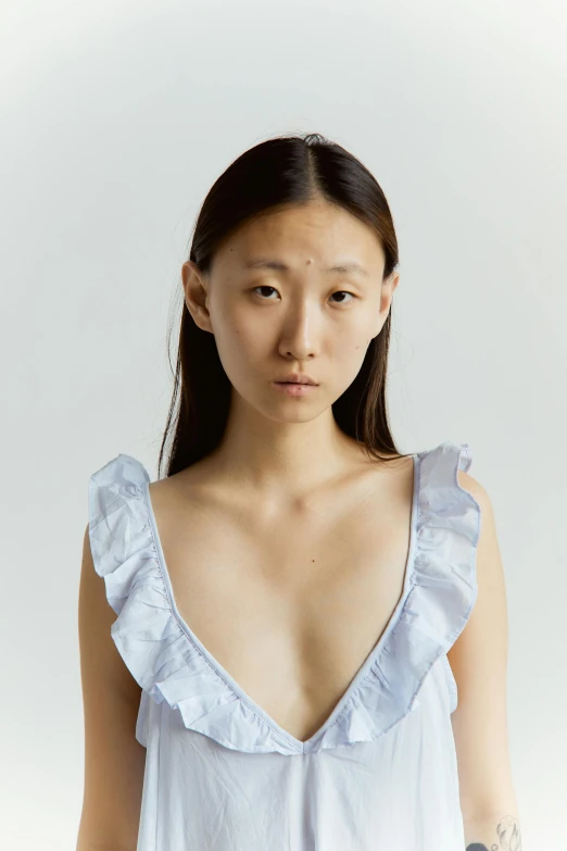 a woman standing in front of a white background, inspired by Xu Xi, trending on reddit, gutai group, wearing a low cut tanktop, pale blue faces, frill, editorial image