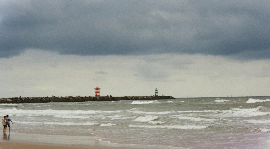 a couple of people standing on top of a sandy beach, by Jan Dirksz Both, lighthouse, overcast weather, rough waters, a green