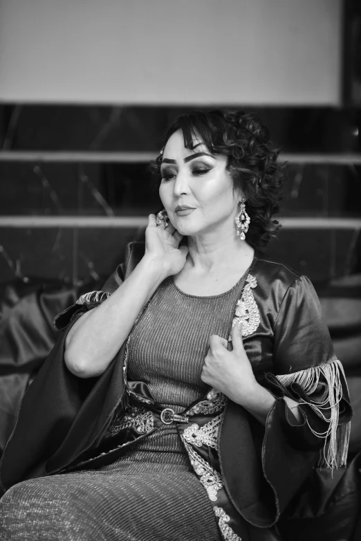 a woman sitting on a couch talking on a cell phone, a black and white photo, inspired by Lubna Agha, pexels contest winner, arabesque, singer in the voice show, in robes, posing elegantly over the camera, traditional makeup
