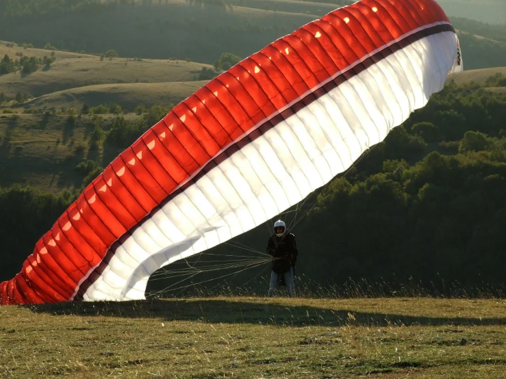 a man that is standing in the grass with a parachute, pexels contest winner, hurufiyya, white and red color scheme, over the hills, seen from the side, back - lit