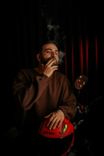 a man sitting on a motorcycle smoking a cigarette, an album cover, pexels, hurufiyya, mac miller, standing in a dimly lit room, nug pic, with red haze