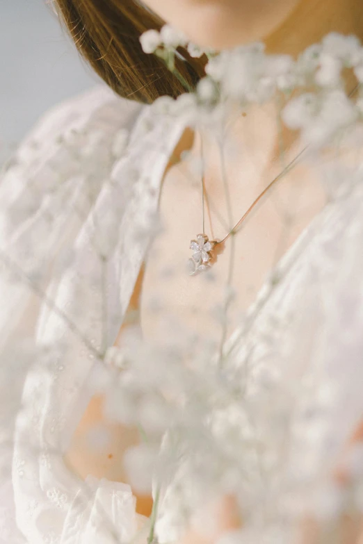 a close up of a woman holding a flower, wearing several pendants, ethereal and dreamy theme, gypsophila, subtle detailing