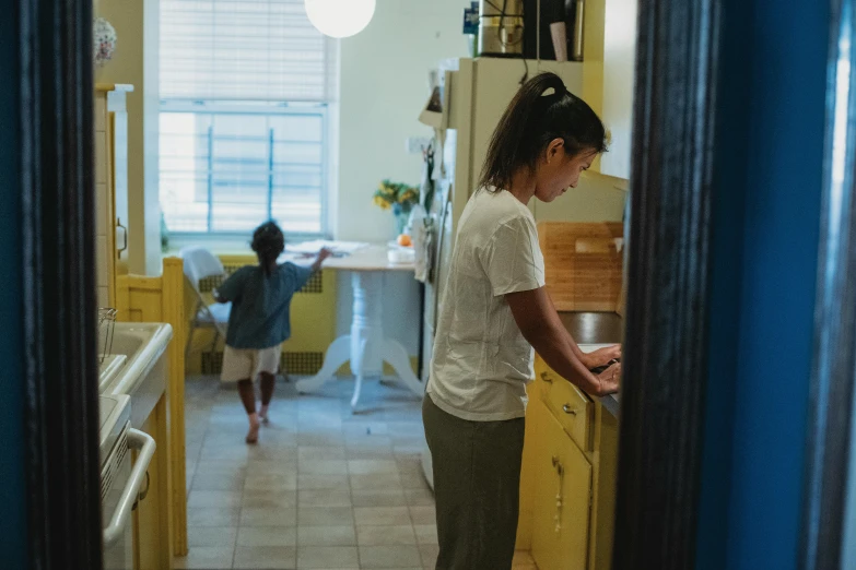 a woman standing in a kitchen next to a sink, by Liza Donnelly, pexels contest winner, with a kid, working on her laptop, zeen chin and farel dalrymple, walking to the right