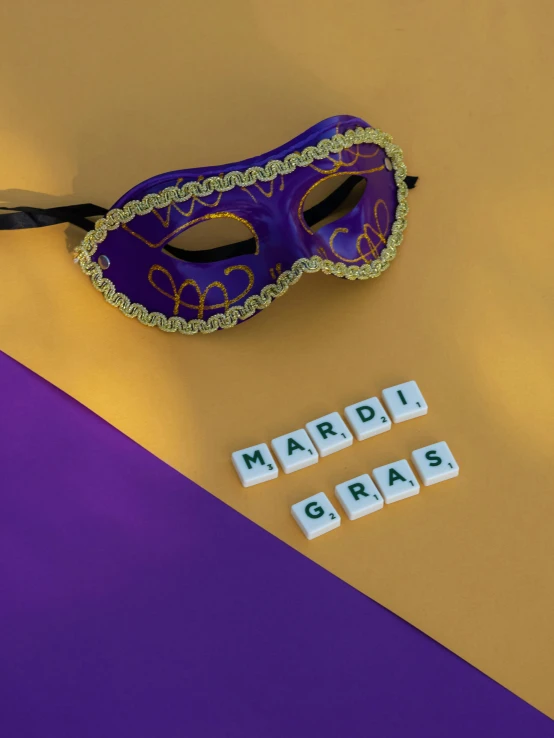 a purple and gold mardi gras mask next to scrabbles, a photo, trending on pexels, square, ((purple)), may)