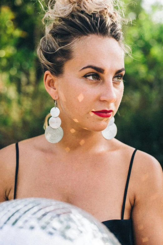 a woman in a black dress holding a silver ball, a portrait, by Niko Henrichon, pexels, multiple earrings, a beautiful woman in white, sydney hanson, her face in discs