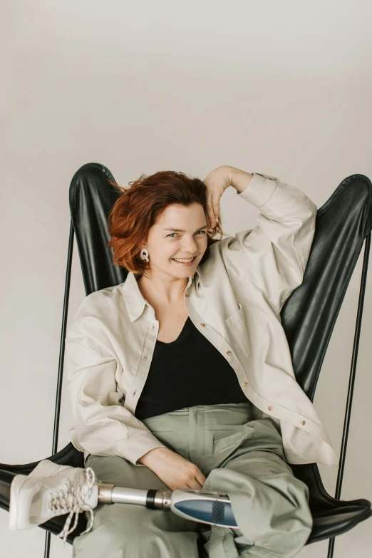 a woman that is sitting in a chair, by Grytė Pintukaitė, trending on unsplash, renaissance, white backdrop, she wears a jacket, relaxing and smiling at camera, redhead woman