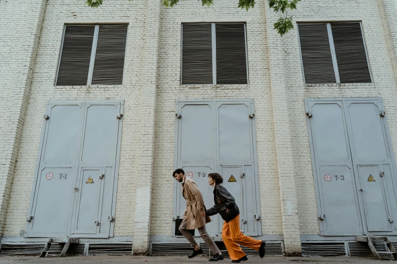 a man and a woman walking in front of a building, pexels contest winner, exiting from a wardrobe, industrial aesthetic, people on the ground, 7 0 s photo