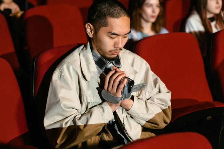 a man sitting in a theater looking at his cell phone, a cartoon, trending on pexels, hyperrealism, japanese live-action movie, praying, wearing jacket, [ theatrical ]