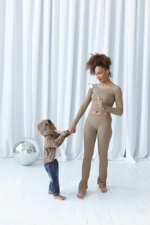 a woman holding the hand of a small child, inspired by The Family Circus, brown pants, doja cat, wearing a track suit, twirls and curves