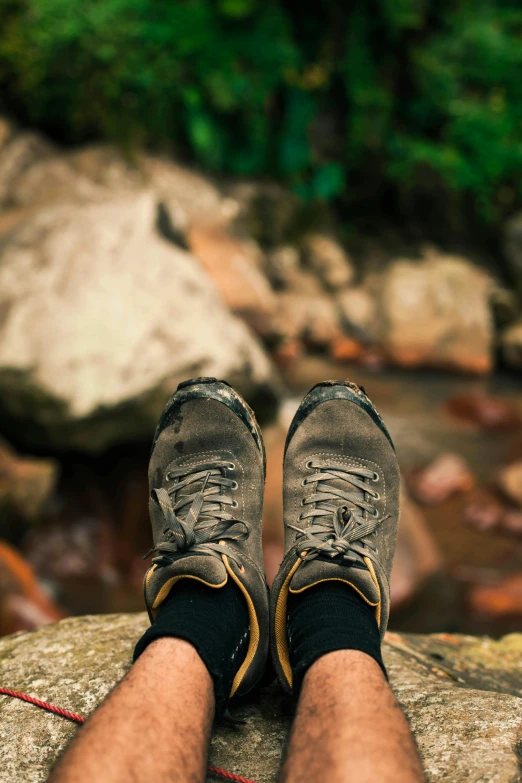 a man sitting on top of a rock next to a river, shoes, detailed legs looming over you, trekking in a forest, screensaver