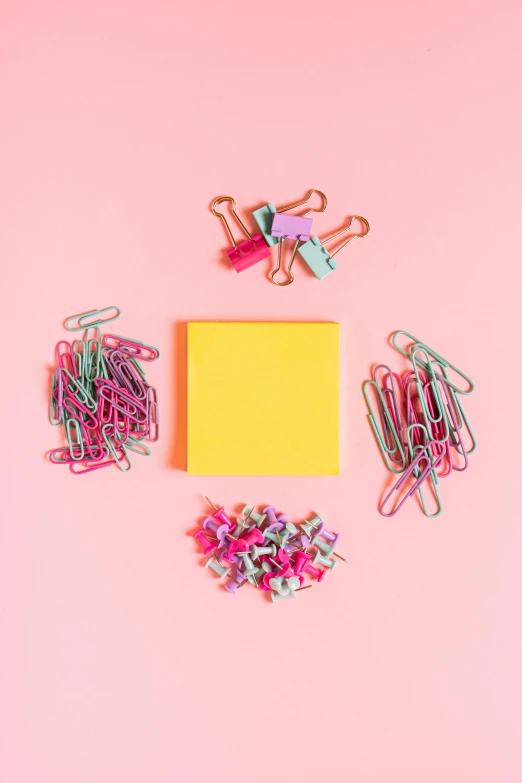 a yellow piece of paper surrounded by colorful paper clips on a pink background, an album cover, by Nicolette Macnamara, trending on pexels, color field, 15081959 21121991 01012000 4k, knolling, pastel pink neon, color picture