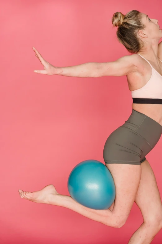 a woman jumping in the air with a blue ball, a colorized photo, by Rachel Reckitt, trending on pexels, arabesque, thigh gap, pink and teal, bent over posture, physical : tinyest midriff ever