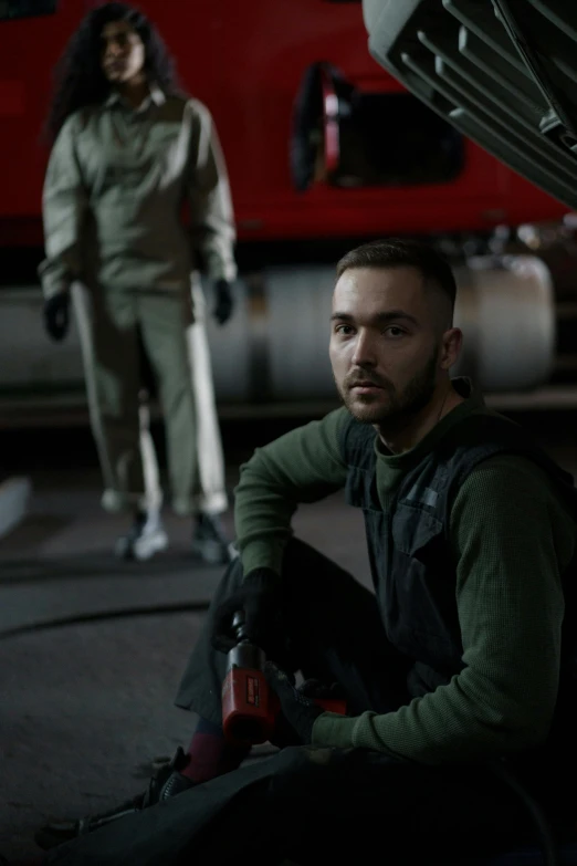 a man sitting on the ground next to a car, charlie cox, wearing human air force jumpsuit, worksafe. cinematic, artem chebokha