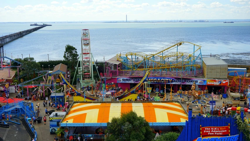 a carnival filled with lots of people next to the ocean, adventure playground, yellow, looking down on the view, multicoloured