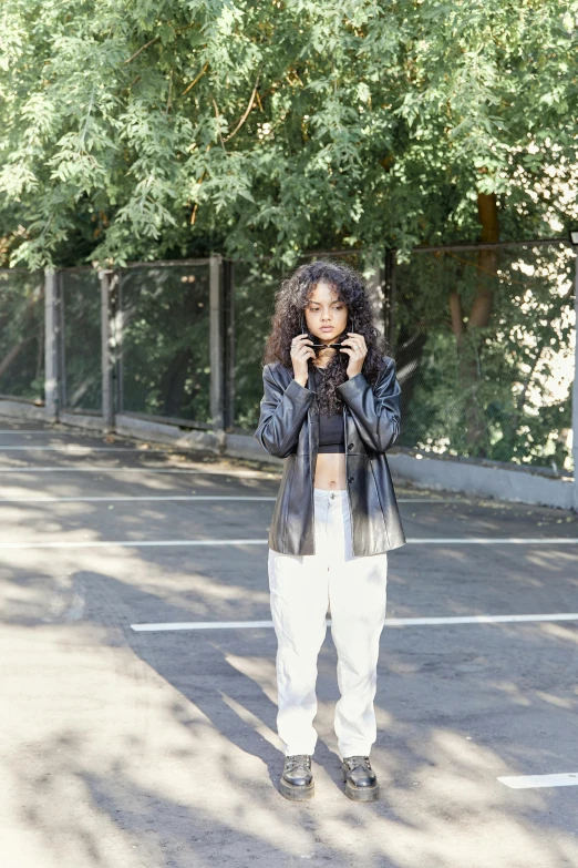 a woman standing in a parking lot talking on a cell phone, an album cover, by Cosmo Alexander, unsplash, wearing a track suit, long black curly hair, leather clothing, various poses shooting photos