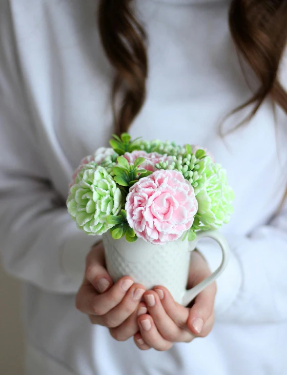 a close up of a person holding a cup with flowers in it, made out of sweets, pink and green, detailed product shot, modeled