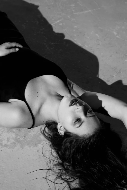 a black and white photo of a woman laying on the ground, inspired by Max Dupain, unsplash, photorealism, still from a music video, sun overhead, barbara palvin, kat dennings