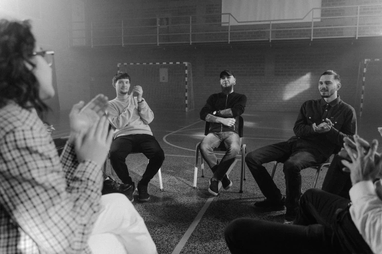 a group of people sitting on top of a basketball court, a black and white photo, pexels, realism, eminem, sitting on a chair, telling stories, secret cypher