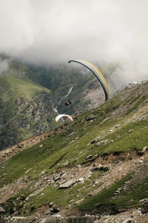 a person paragliding in the mountains on a cloudy day, by Werner Andermatt, hurufiyya, nat geo, parachutes, india, back