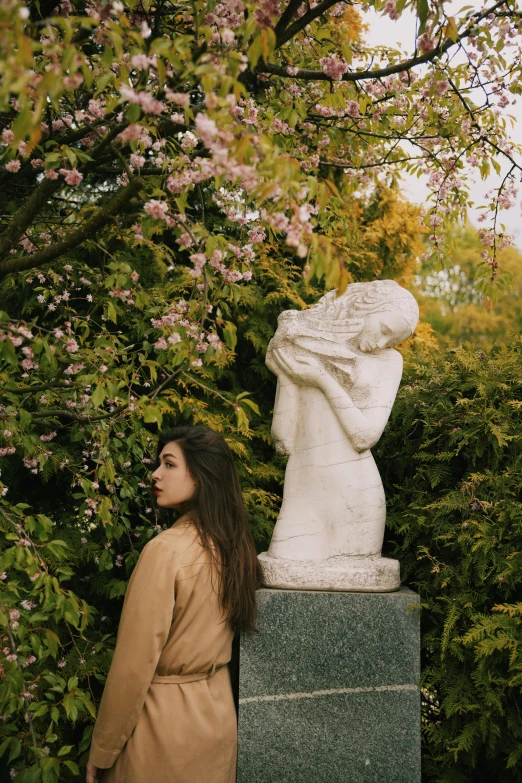 a woman standing next to a statue in a park, unsplash, art nouveau, blossoms, marble sculptures, instagram photo, hiding