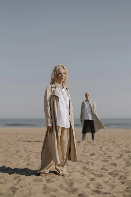 a woman standing on top of a sandy beach, by Matija Jama, renaissance, he is wearing a trenchcoat, older woman, promo still, a blond