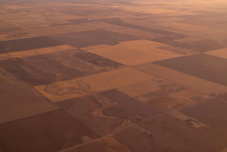 an airplane that is flying in the sky, an album cover, unsplash, precisionism, drought, patchwork, farms, brown