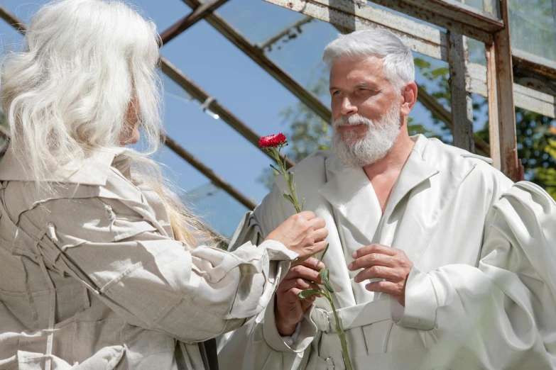 a man standing next to a woman holding a rose, inspired by Petrus Christus, pexels contest winner, long white hair and white beard, in bloom greenhouse, wearing long silver robes, haeckel and alasdair gray