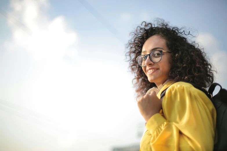 a close up of a person with a backpack, wavy hair yellow theme, girl wearing round glasses, african ameera al taweel, on a bright day