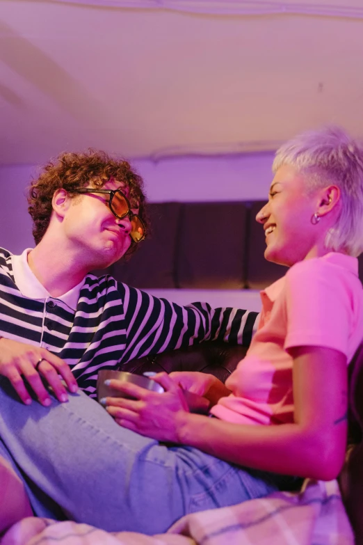 a man and a woman sitting on a bed, a cartoon, pexels, cinematic neon uplighting, wearing small round glasses, gay rights, on a couch