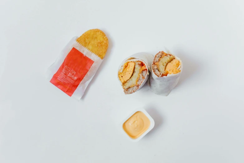 a sandwich and some condiments on a white surface, a picture, unsplash, dau-al-set, mcdonalds wrapper on table, white and orange, high - angle view, nugget