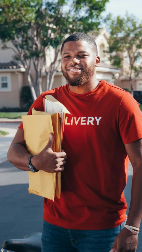 a man in a red shirt standing next to a motorcycle, pexels contest winner, renaissance, delivering mail, non-binary, brown skin man with a giant grin, close up half body shot