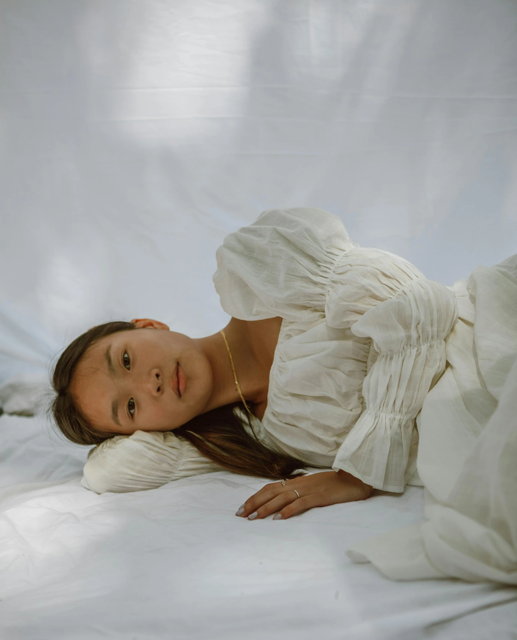 a woman in a white dress laying on a bed, inspired by Juan Luna, pexels contest winner, portrait of a japanese teen, puff sleeves, album cover, taken in 2022