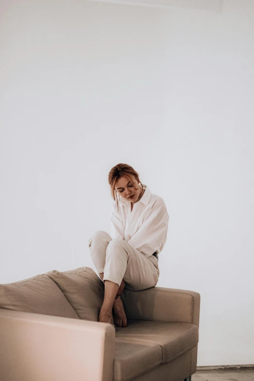 a woman sitting on top of a couch in a living room, by Matija Jama, trending on pexels, minimalism, wearing white pajamas, plain background, unsimulated real emotions, uwu