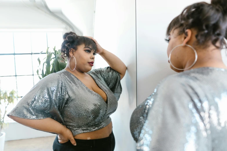 a woman standing in front of a mirror, trending on pexels, alluring plus sized model, grey and silver, sequin top, vibrant scene