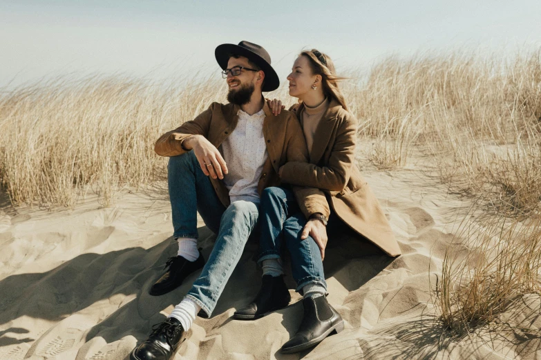 a man and a woman sitting in the sand, a portrait, unsplash contest winner, straw hat and overcoat, hipster dad, supportive, instagram post