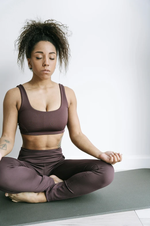 a woman sitting in a lotus position on a yoga mat, by Nina Hamnett, trending on pexels, renaissance, wearing a cropped tops, muted browns, ashteroth, two piece workout clothes