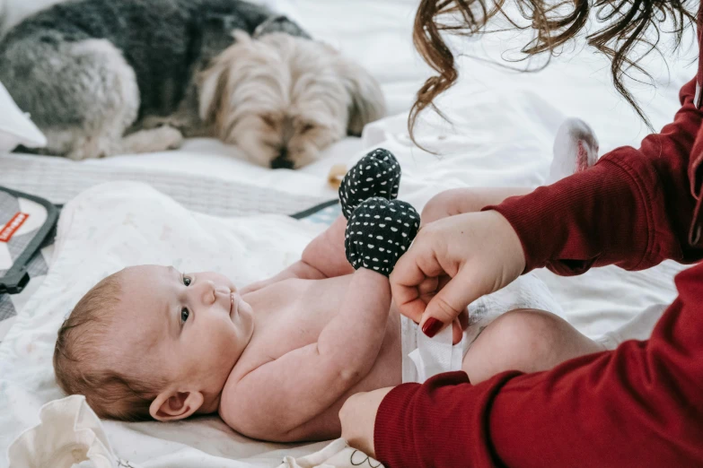 a baby laying on top of a bed next to a dog, by Nina Hamnett, pexels contest winner, incoherents, holding a syringe, holding hands, bows, lachlan bailey