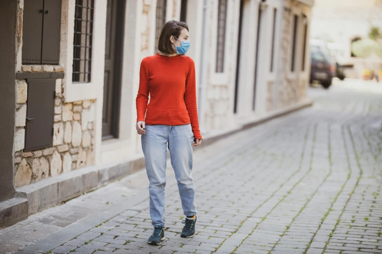 a woman wearing a face mask walks down a cobblestone street, pexels, red sweater and gray pants, avatar image, sport clothing, blue and orange