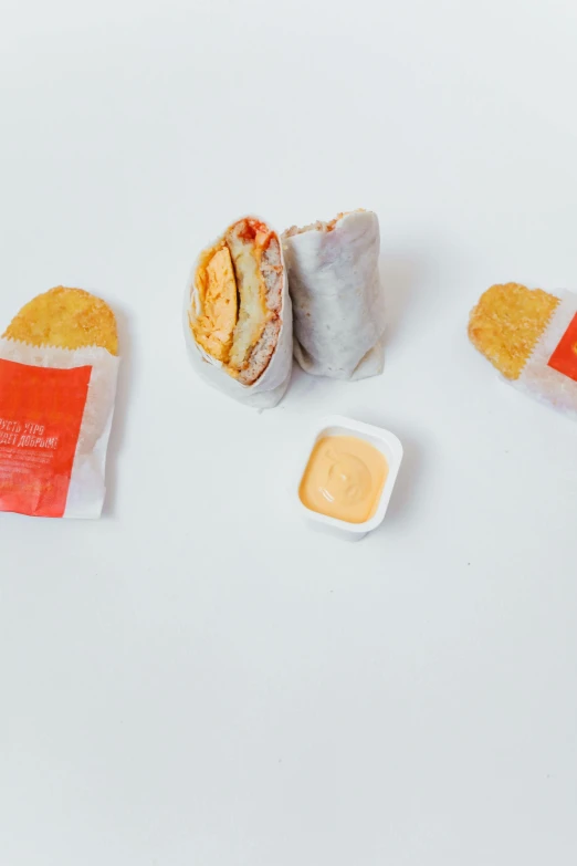 a couple of sandwiches sitting on top of a white table, mcdonalds wrapper on table, orange and white, deconstructed, various sizes